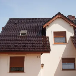 Dom jednorodzinny w Niepruszewie z brązową dachówką karpiówką i oknem dachowym, widoczne rolety zewnętrzne.