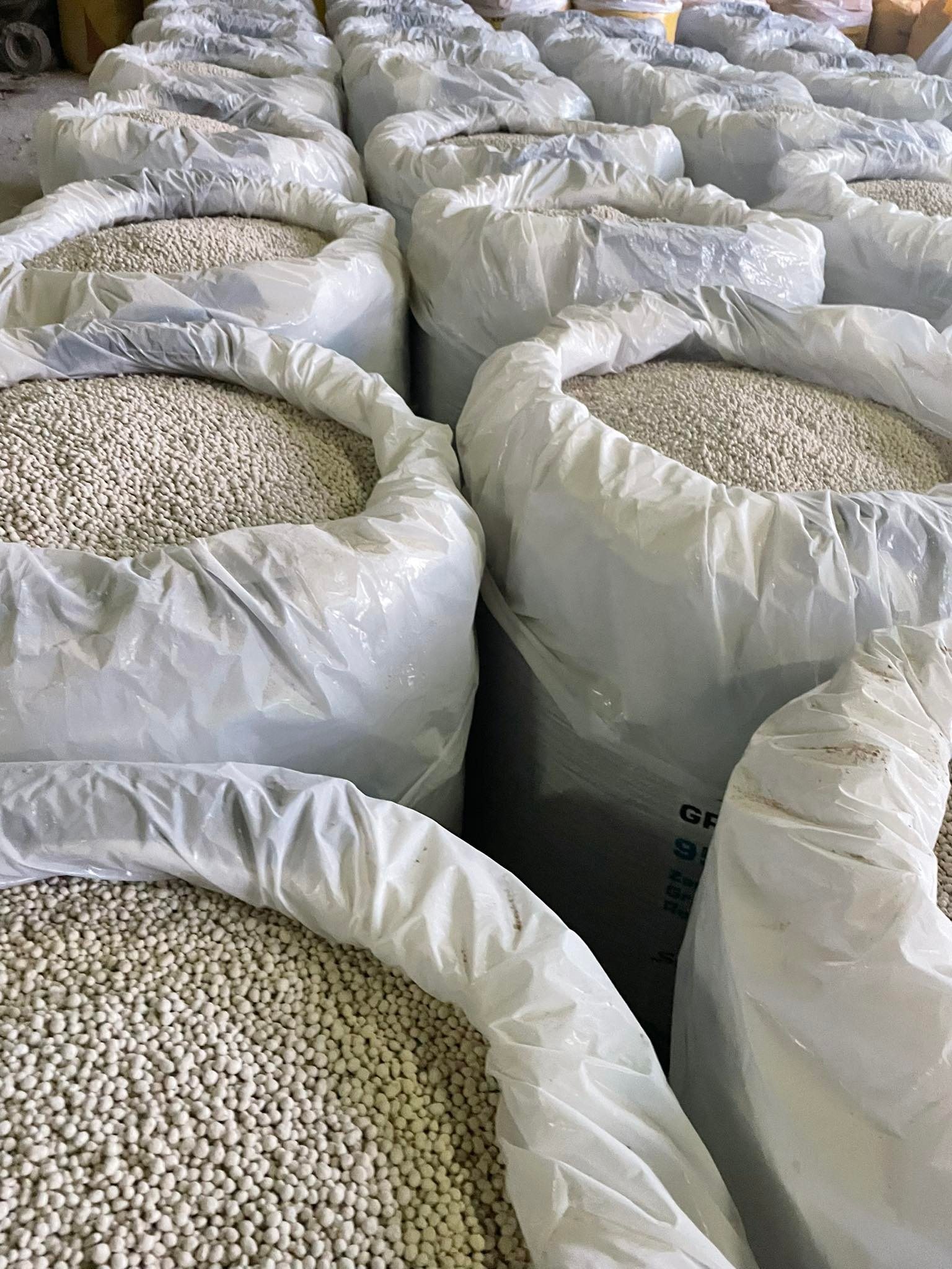 Wiele worków wypełnionych białymi granulkami nawozu, ułożonych rzędami w magazynie.