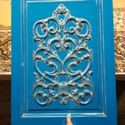 Błękitny front meblowy z ornamentem w stylu retro, trzymany w dłoni, ukazujący detale zdobienia.