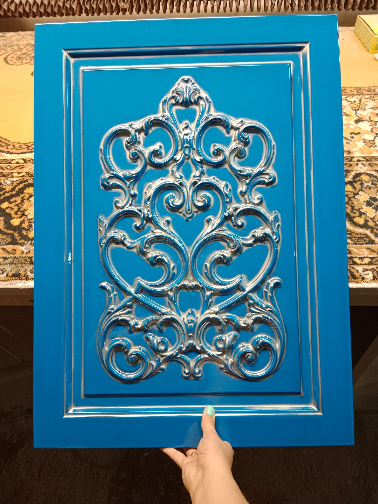 Błękitny front meblowy z ornamentem w stylu retro, trzymany w dłoni, ukazujący detale zdobienia.