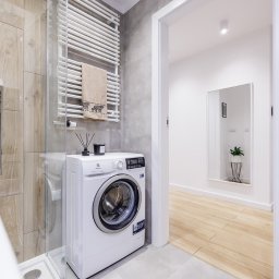 Paweł Malejky - Fotografia - Nowoczesna łazienka z kabiną prysznicową, pralką Electrolux, grzejnikiem drabinkowym z ręcznikiem w panterkę i aromaterapią. W tle widoczne lustro w korytarzu.