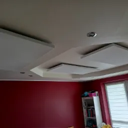 Sufit podwieszany z panelami akustycznymi i wpuszczonymi oprawami oświetleniowymi, widok od dołu, ściana pomalowana na bordowo.