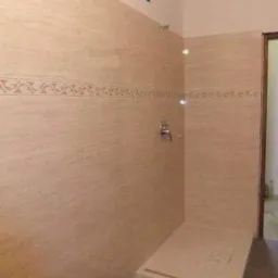 Wykończona kabina prysznicowa z beżowymi płytkami imitującymi kamień, dekoracyjnym pasem płytek z ornamentem i zamontowaną baterią.