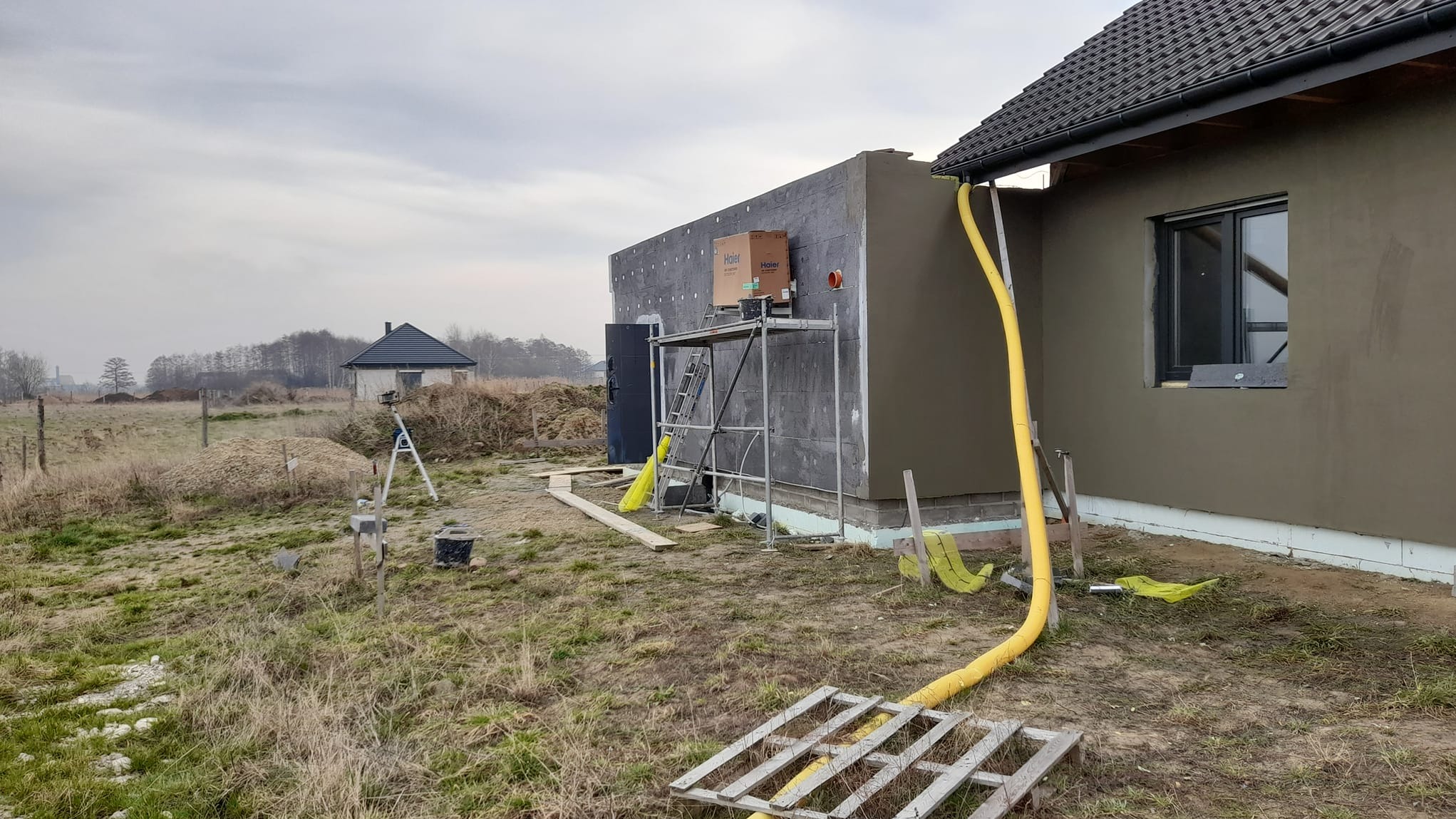 Dom w trakcie ocieplania, widoczne rusztowanie, styropian, żółty wąż wentylacyjny i pudełko z klimatyzatorem na rusztowaniu.