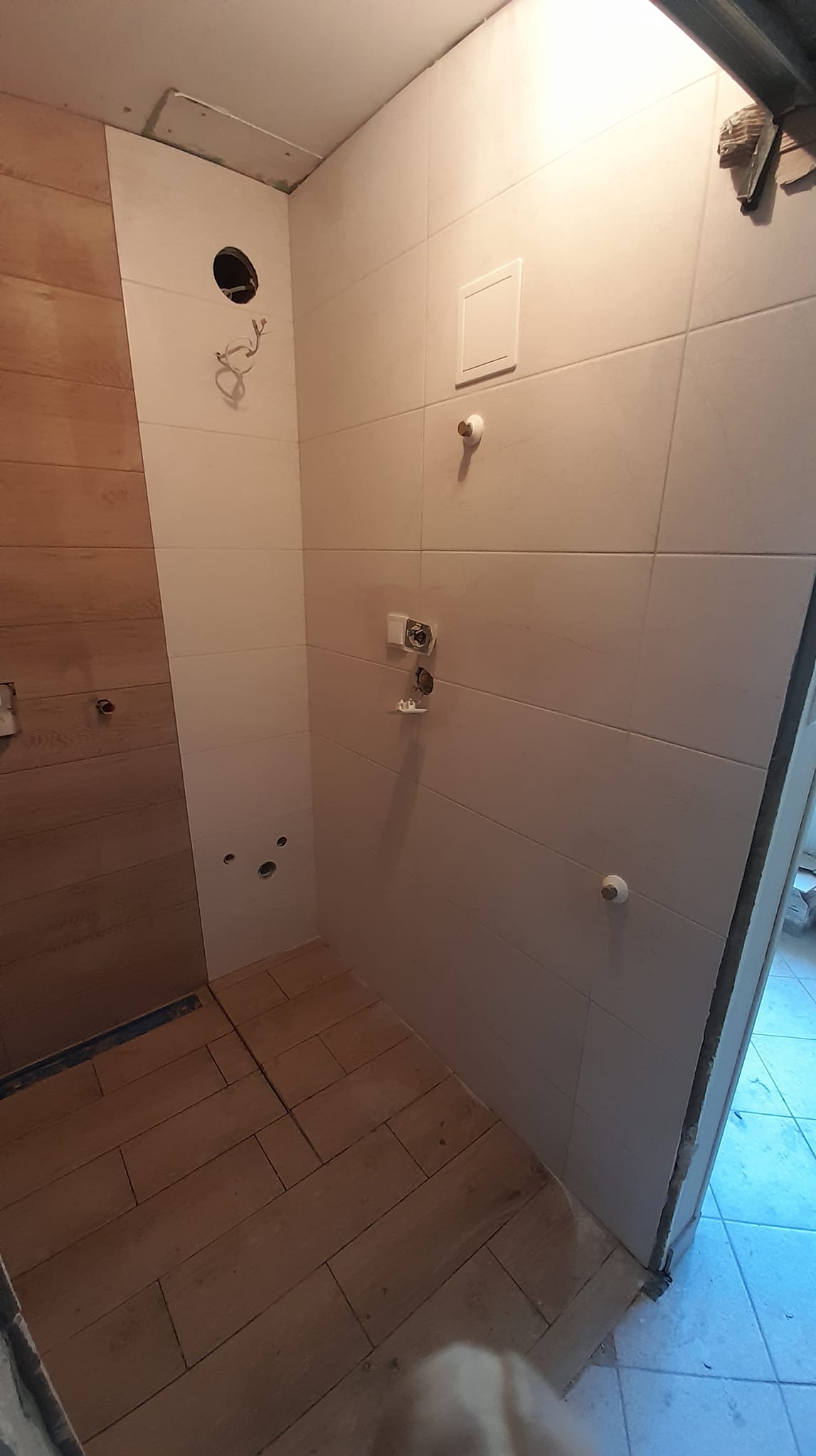 Łazienka w trakcie remontu, widoczne płytki na ścianach, drewnopodobna podłoga, przygotowane punkty instalacyjne, brak armatury.