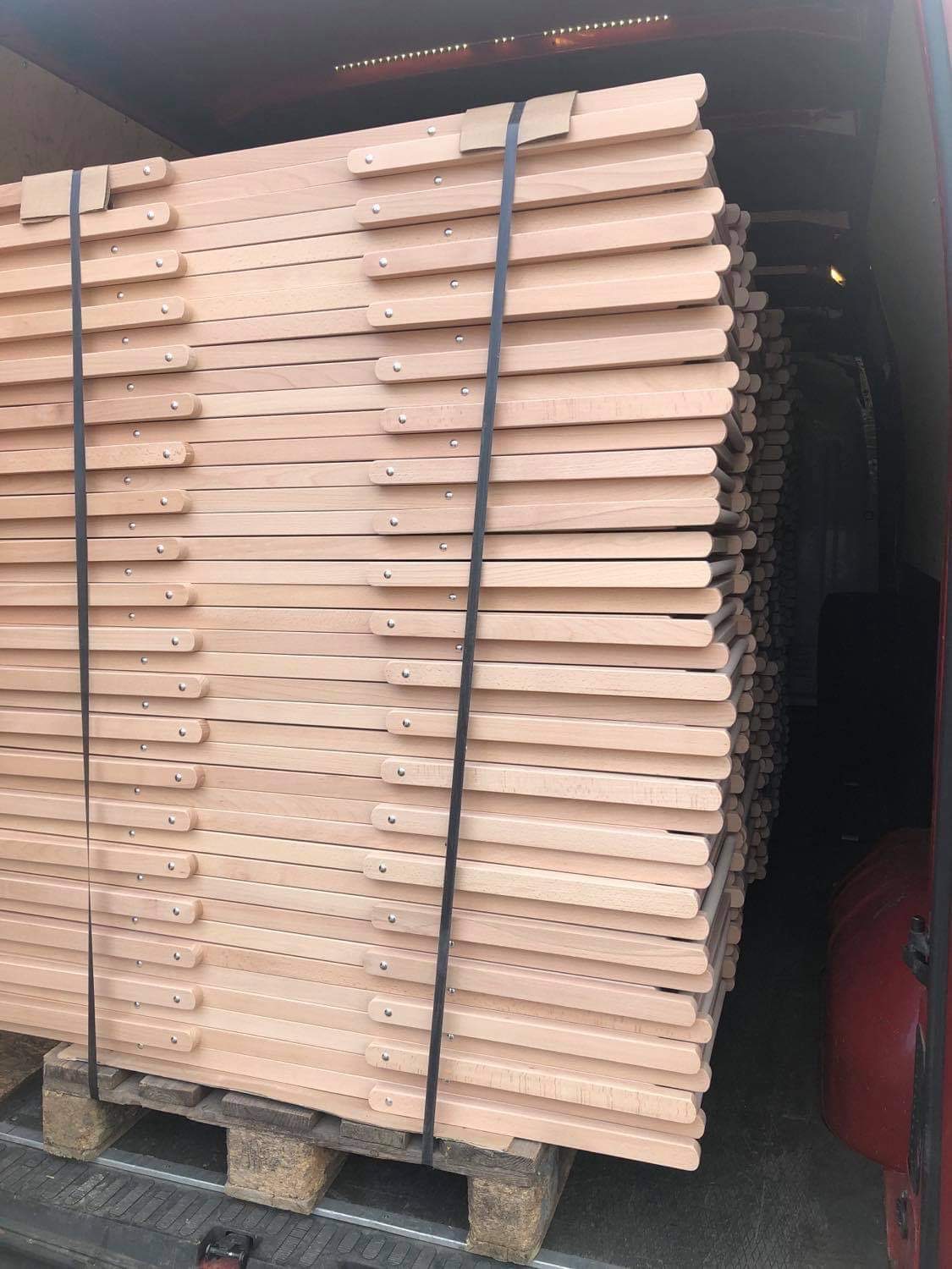 Stos drewnianych, składanych leżaków zabezpieczonych pasami transportowymi na palecie wewnątrz pojazdu dostawczego.
