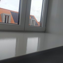 Artur Walenciuk - Błyszczący, świeżo pomalowany biały parapet wewnętrzny z widokiem na dach z czerwoną dachówką i panele słoneczne za oknem.