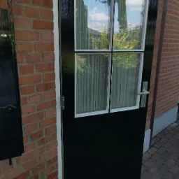 Ciemna, błyszcząca rama okna z szybami i zasłonami, wbudowana w ceglaną ścianę zewnętrzną budynku.