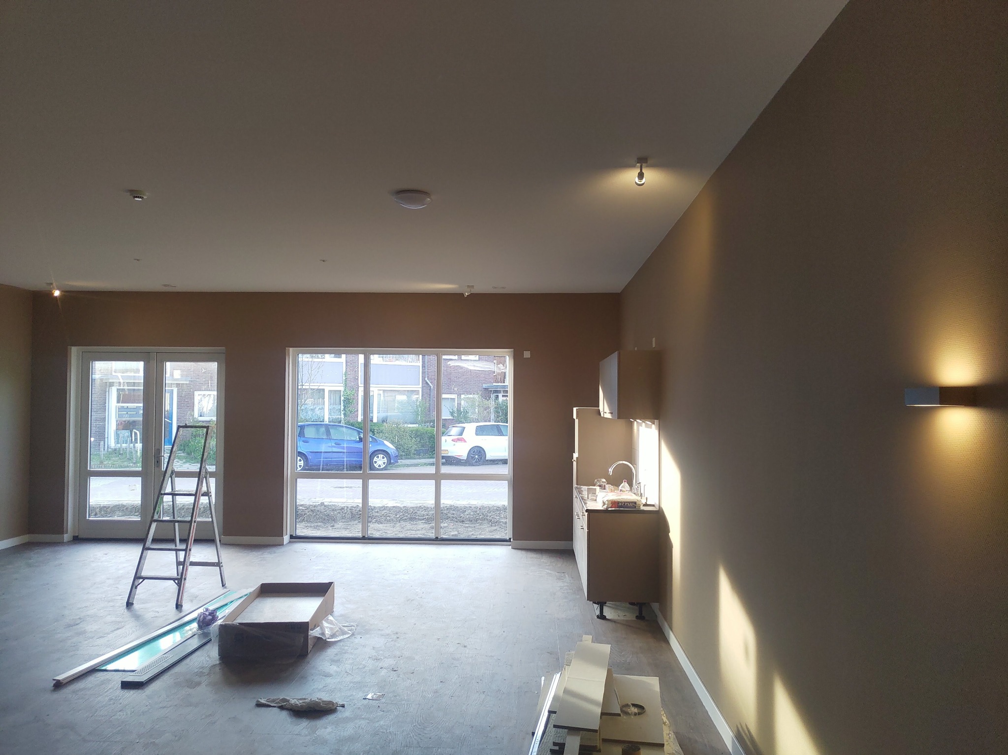 Wnętrze w trakcie prac wykończeniowych, z drabina opartą o okno, widoczne elementy zabudowy kuchennej i przygotowane listwy przypodłogowe.