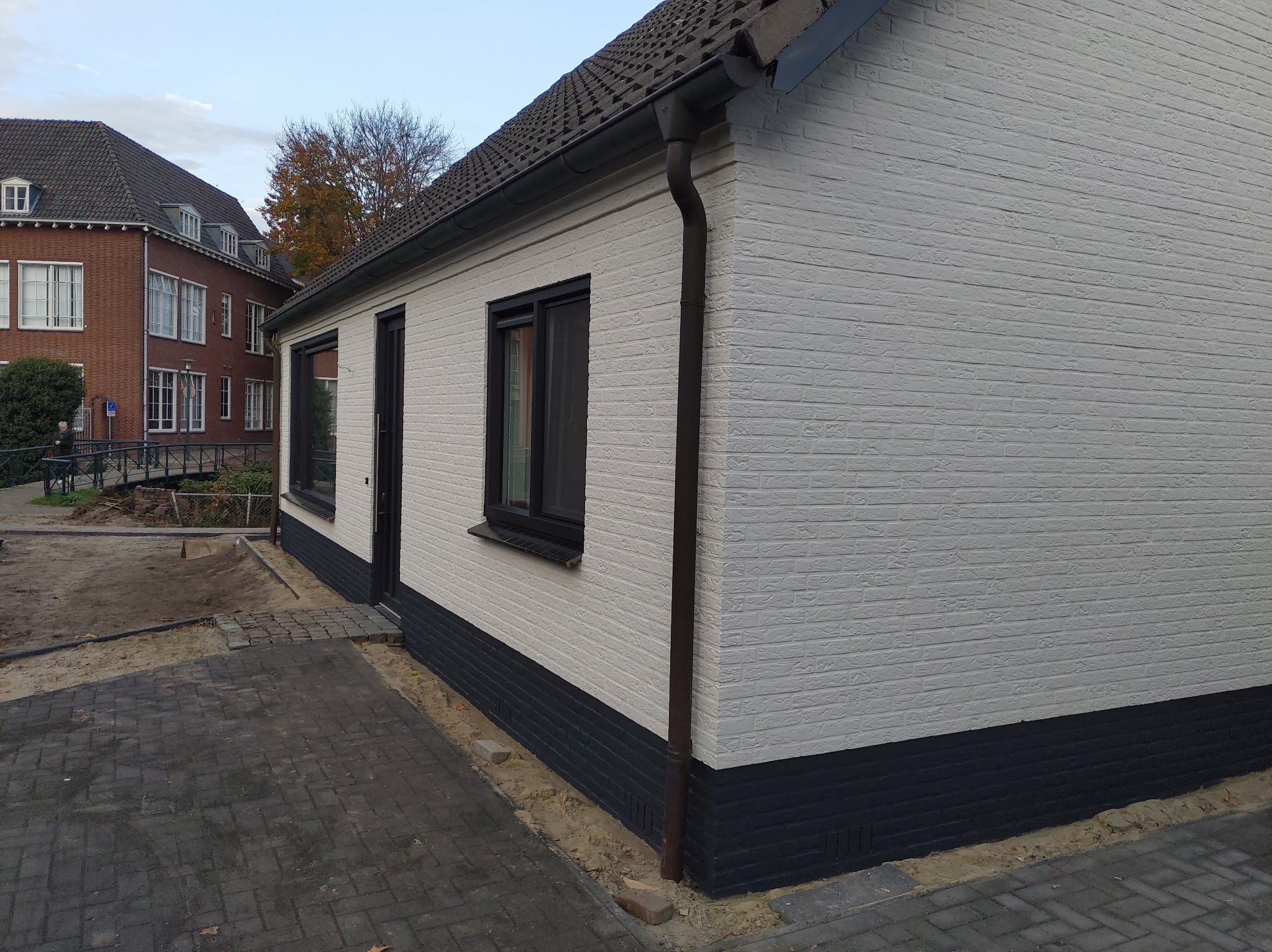 Odnowiona elewacja domu w Łęcznej, z białymi ścianami i ciemnym cokołem, widok z zewnątrz na tle chodnika z kostki brukowej i sąsiedniego budynku.
