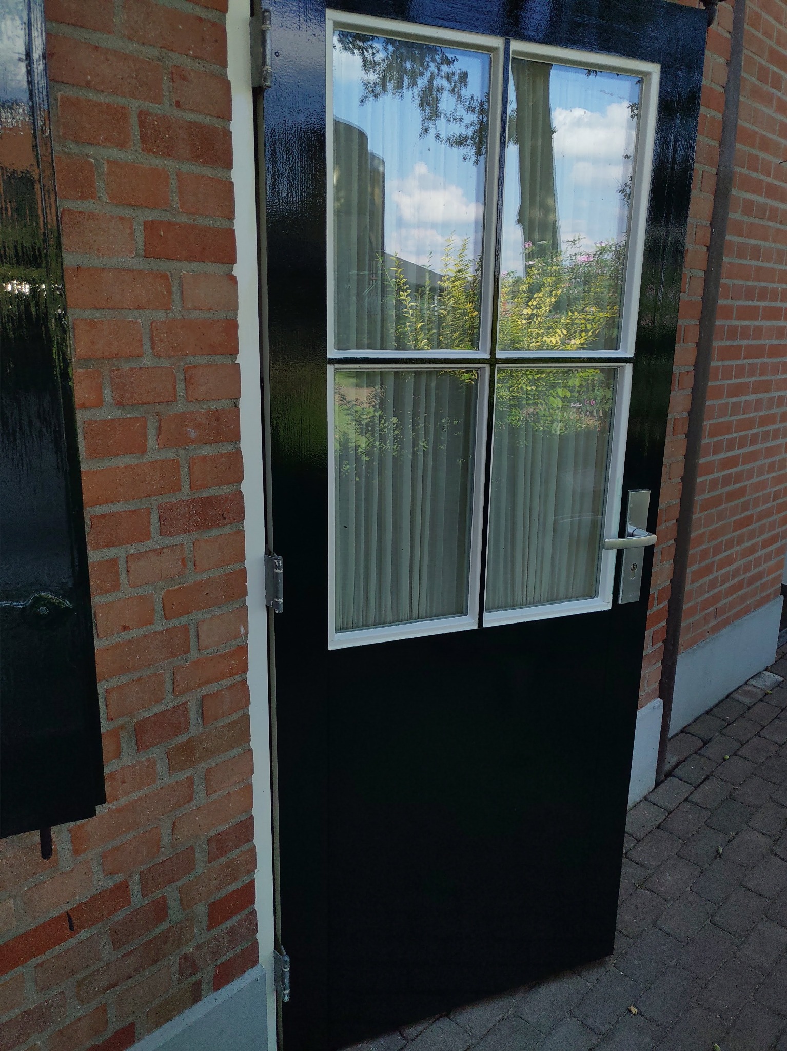 Ciemna, błyszcząca rama okna z szybami i zasłonami, wbudowana w ceglaną ścianę zewnętrzną budynku.