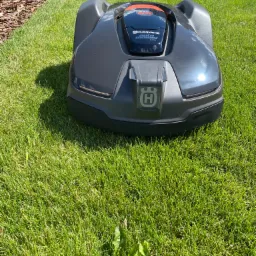 Szary robot koszący Husqvarna Automower 430X na zielonym trawniku w słoneczny dzień, widoczny fragment krawężnika z korą.