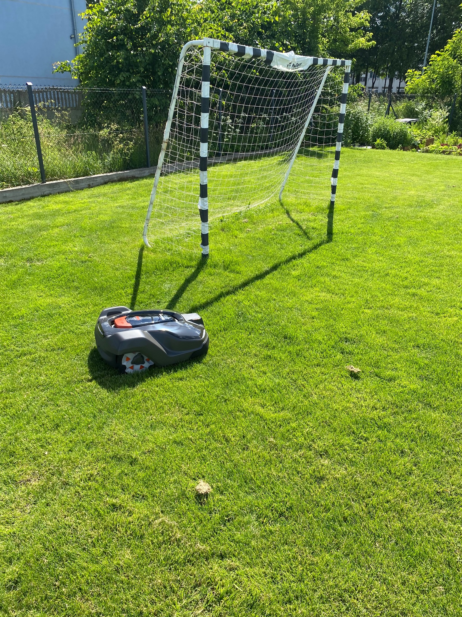 Robot koszący trawnik automatycznie kosi trawę na zielonym boisku z bramką w tle.