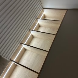 F. H. U. SONIA WIDAJEWICZ - Półki wnękowe z oświetleniem LED, jasne drewno, nowoczesny design, widok z dołu, dekoracyjne listwy ścienne w tle.