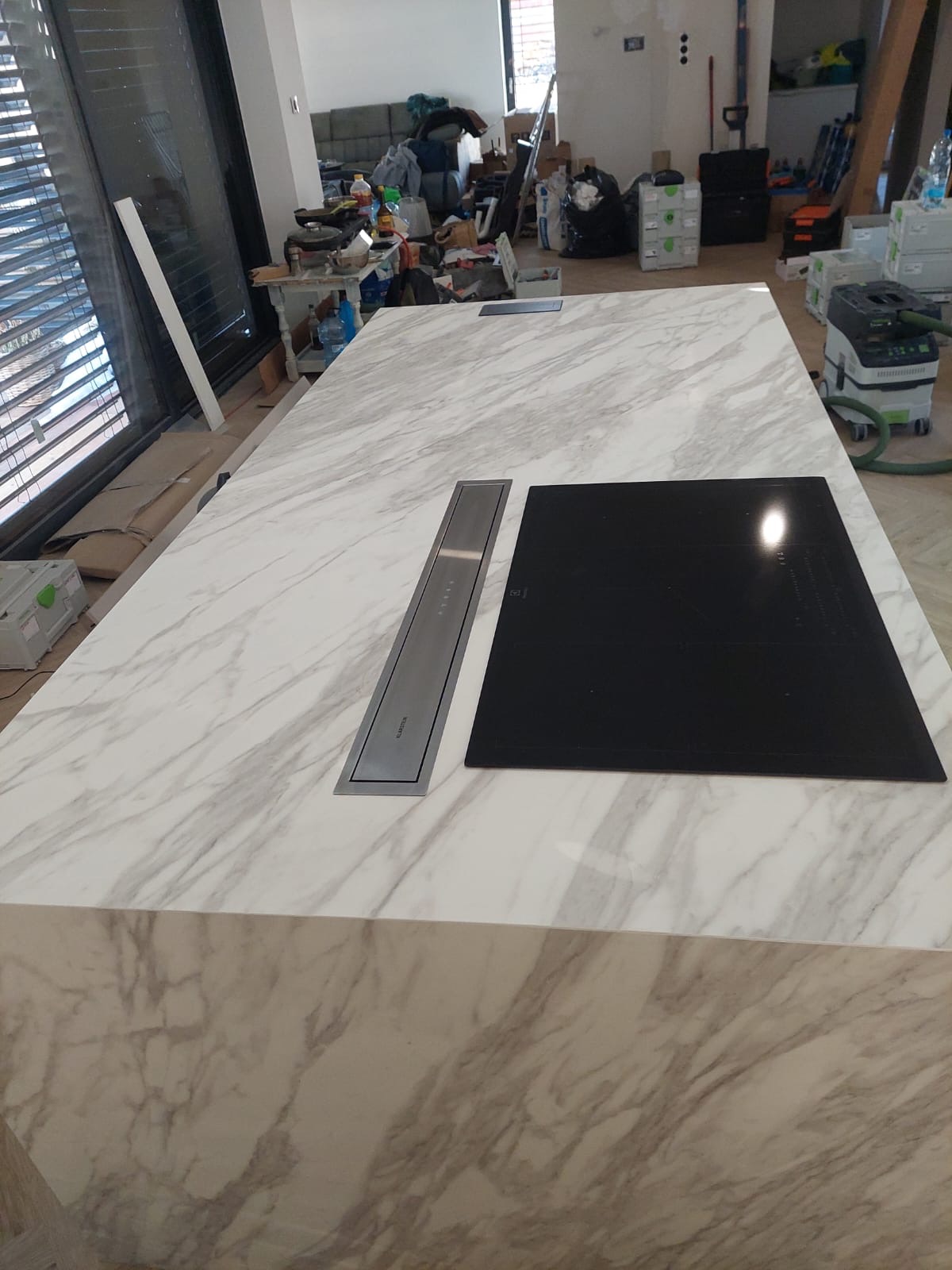 Marmurowy blat wyspy kuchennej w Zabrzu z zamontowaną płytą indukcyjną i pochłaniaczem oparów, widoczne narzędzia i materiały budowlane w tle.