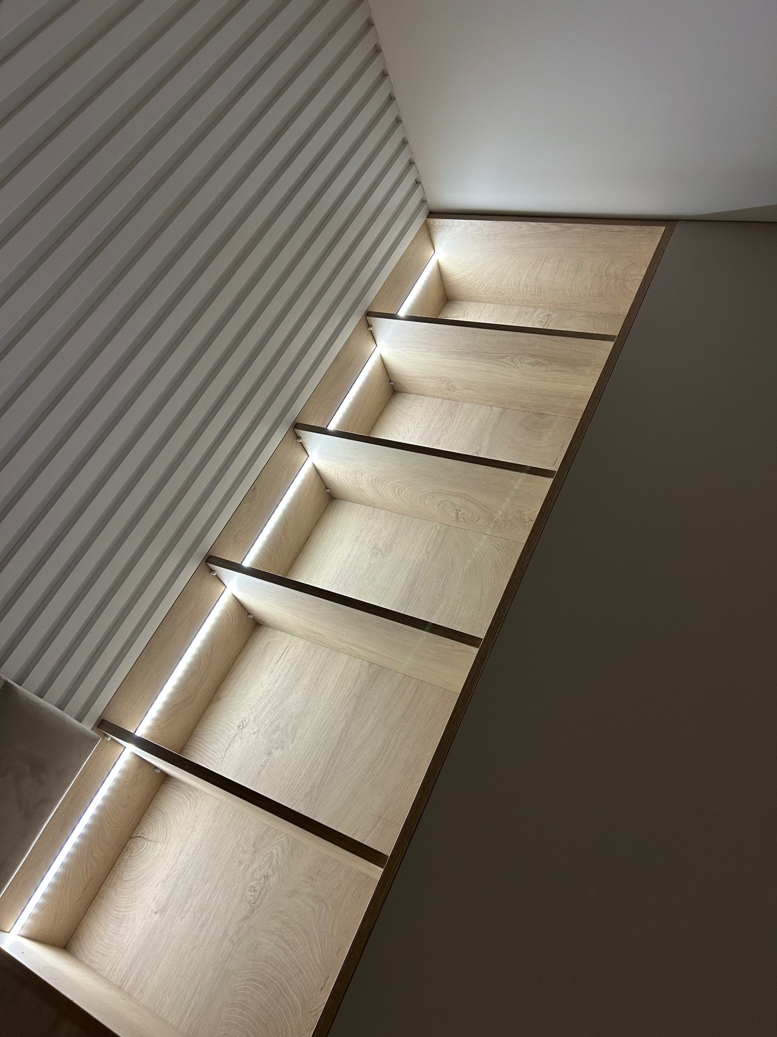 Półki wnękowe z oświetleniem LED, jasne drewno, nowoczesny design, widok z dołu, dekoracyjne listwy ścienne w tle.