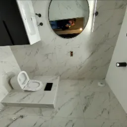 Nowoczesna łazienka z marmurowymi płytkami, okrągłym lustrem z podświetleniem LED i czarną armaturą, widoczna toaleta na podwyższeniu i czarny blat obok