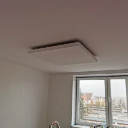 Płyta kartonowo-gipsowa zamontowana na suficie w pokoju z oknem, widoczna drabina malarska i butelka wody na parapecie.