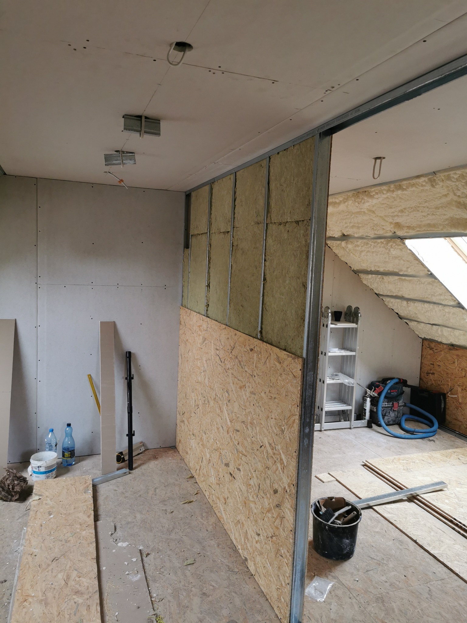 Poddasze w trakcie adaptacji: ściana działowa z izolacją z wełny mineralnej, częściowo obłożona płytą OSB, widoczne profile metalowe, sufit z płyt kartonowo-gipsowych, ocieplone skosy dachu pianą PUR.