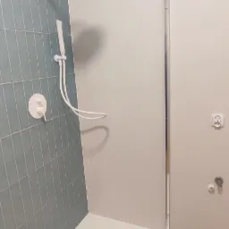 Nowoczesna kabina prysznicowa z błękitnymi płytkami na ścianie, białą armaturą i brodzikiem z odpływem liniowym, widok na fragment podłogi imitującej drewno.