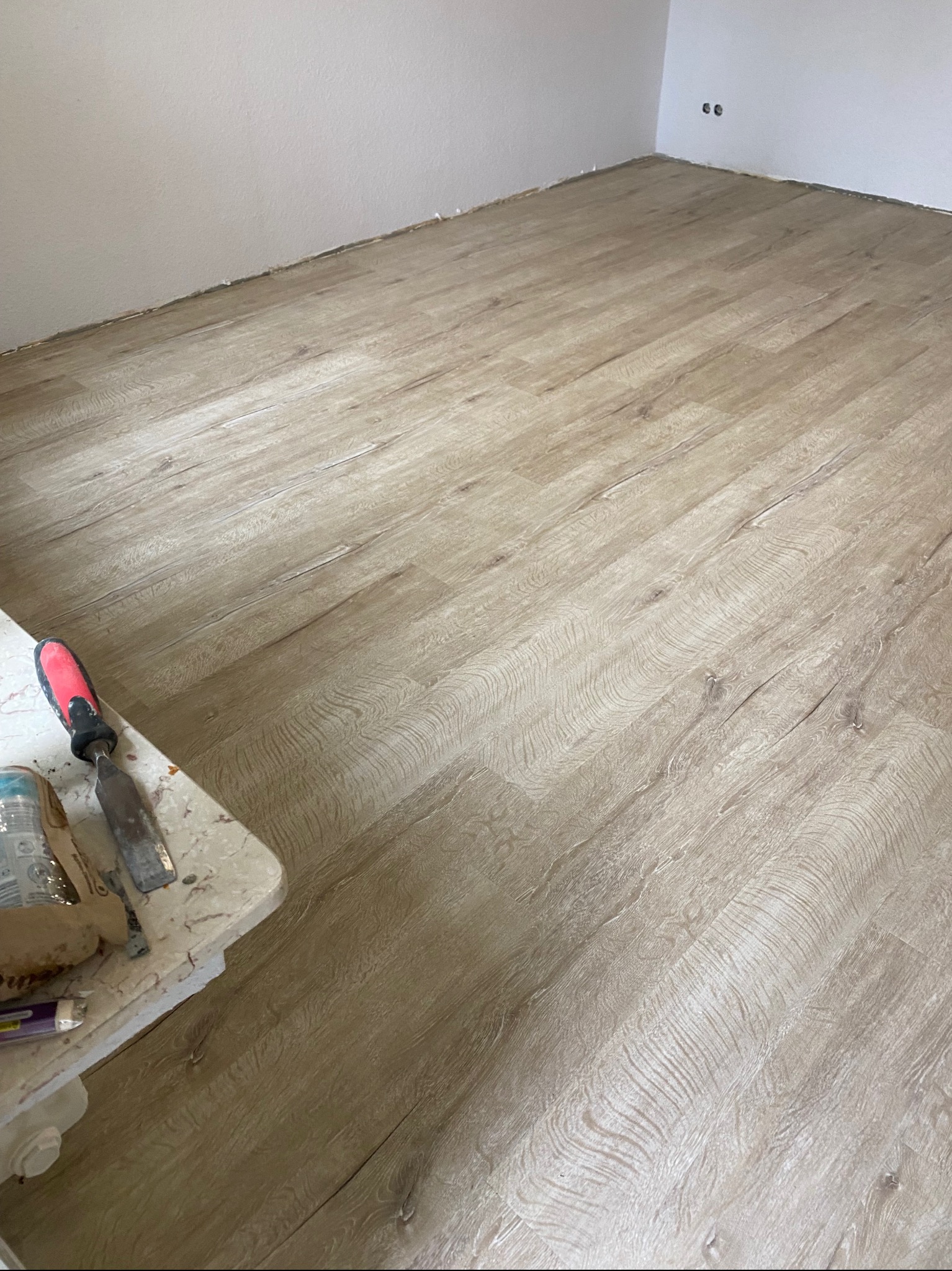 Ułożona podłoga z paneli imitujących drewno, widoczne narzędzia pracy na blacie. Jasne wnętrze, świeżo wykończone ściany. Układanie paneli podłogowych.