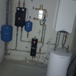 JK Instalacje - Zainstalowany system grzewczy z kotłem wiszącym Termet, zbiornikiem Viessmann i dwoma niebieskimi naczyniami przeponowymi oraz czarnymi elementami armatury, widoczne rury i zawory.