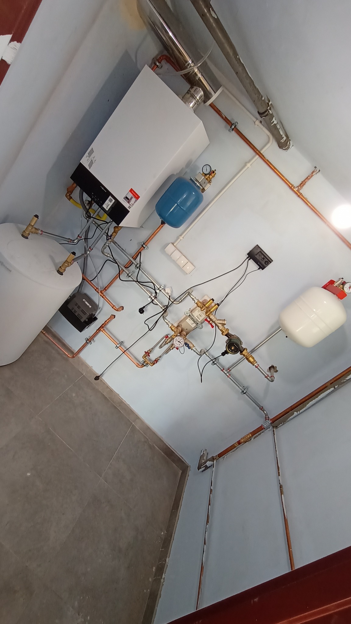 Zmontowana instalacja centralnego ogrzewania z kotłem, zbiornikiem, naczyniami przeponowymi i miedzianymi rurami, widok z dołu.