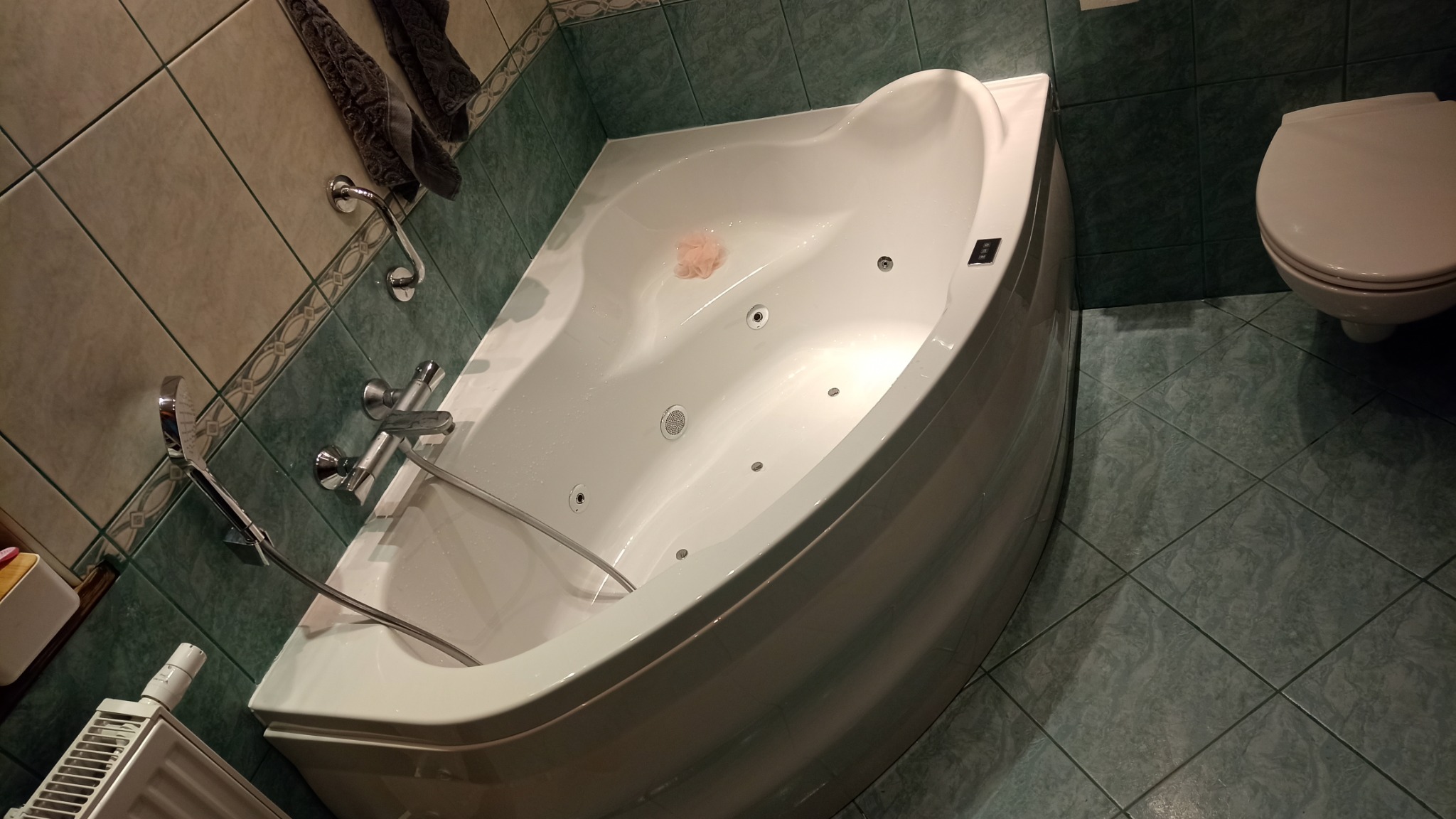 Narożna wanna z hydromasażem, zamontowana w łazience w Wejherowie, z widocznymi dyszami i słuchawką prysznicową, na tle płytek w odcieniach zieleni.