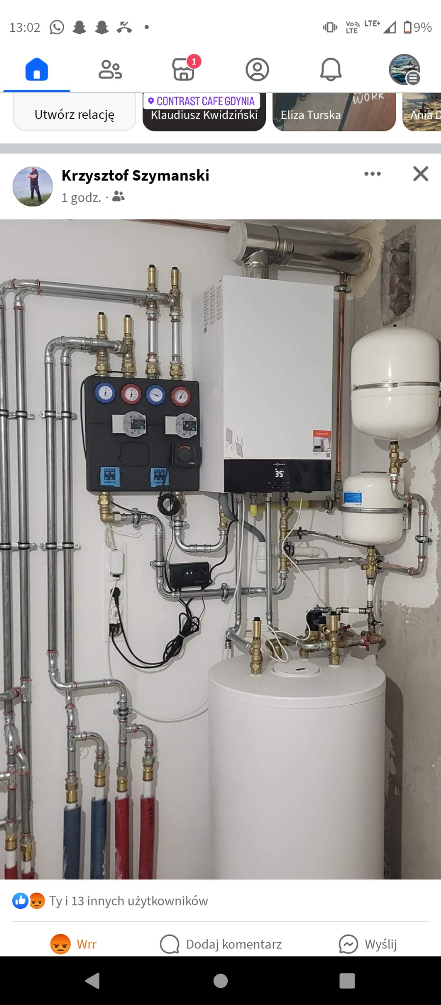 Złożona instalacja grzewcza z kotłem gazowym, zasobnikiem ciepłej wody i rozdzielaczem, rury miedziane i stalowe, manometry na rozdzielaczu, widoczne okablowanie, surowy tynk w tle.