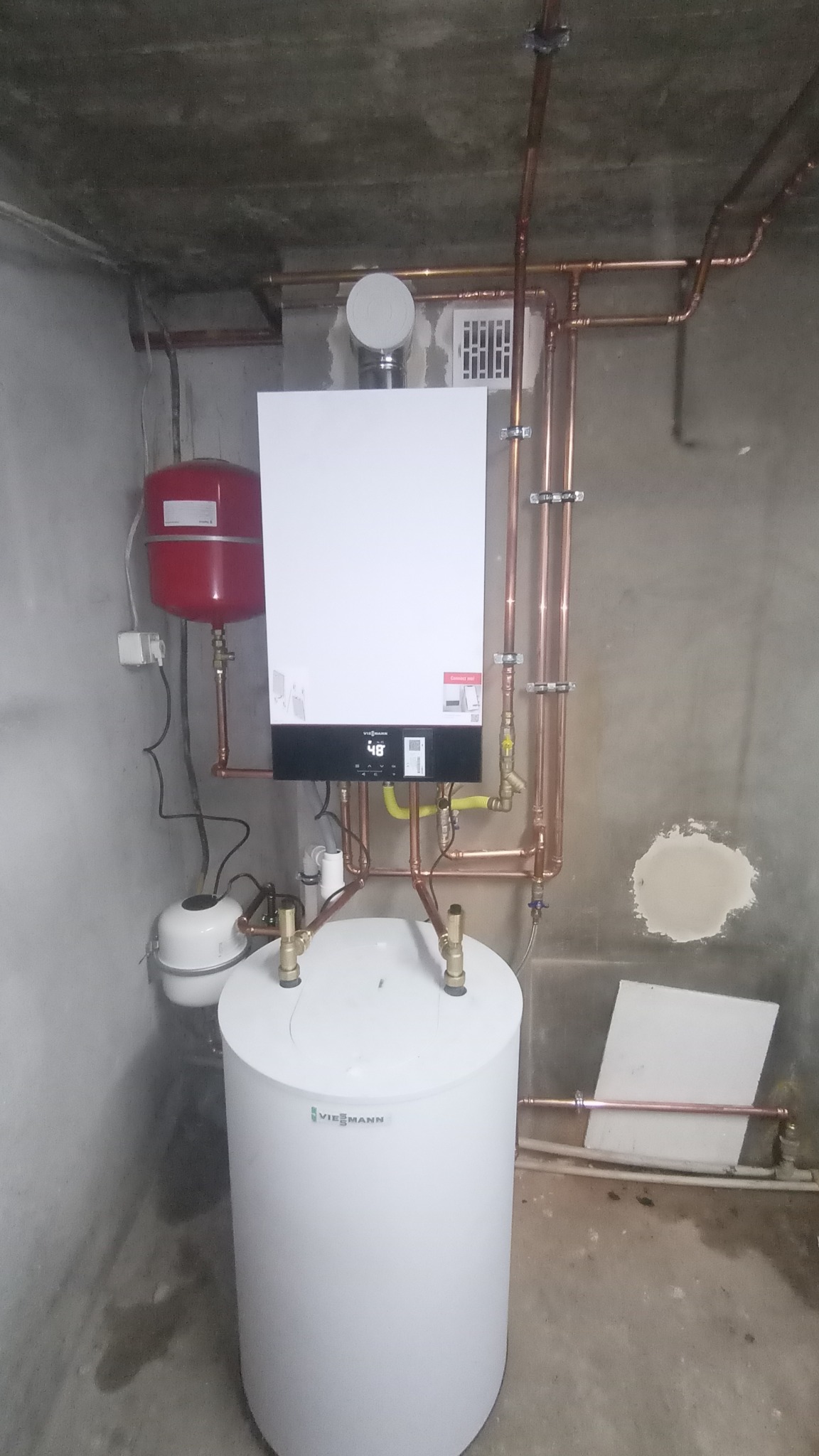 Nowoczesny piec gazowy Viessmann z podłączonym zasobnikiem ciepłej wody i instalacją miedzianą w surowym pomieszczeniu technicznym.