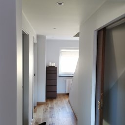 Patryk Sawicki - Korytarz w jasnych barwach z drewnianą podłogą, komodą i drzwiami przesuwnymi.