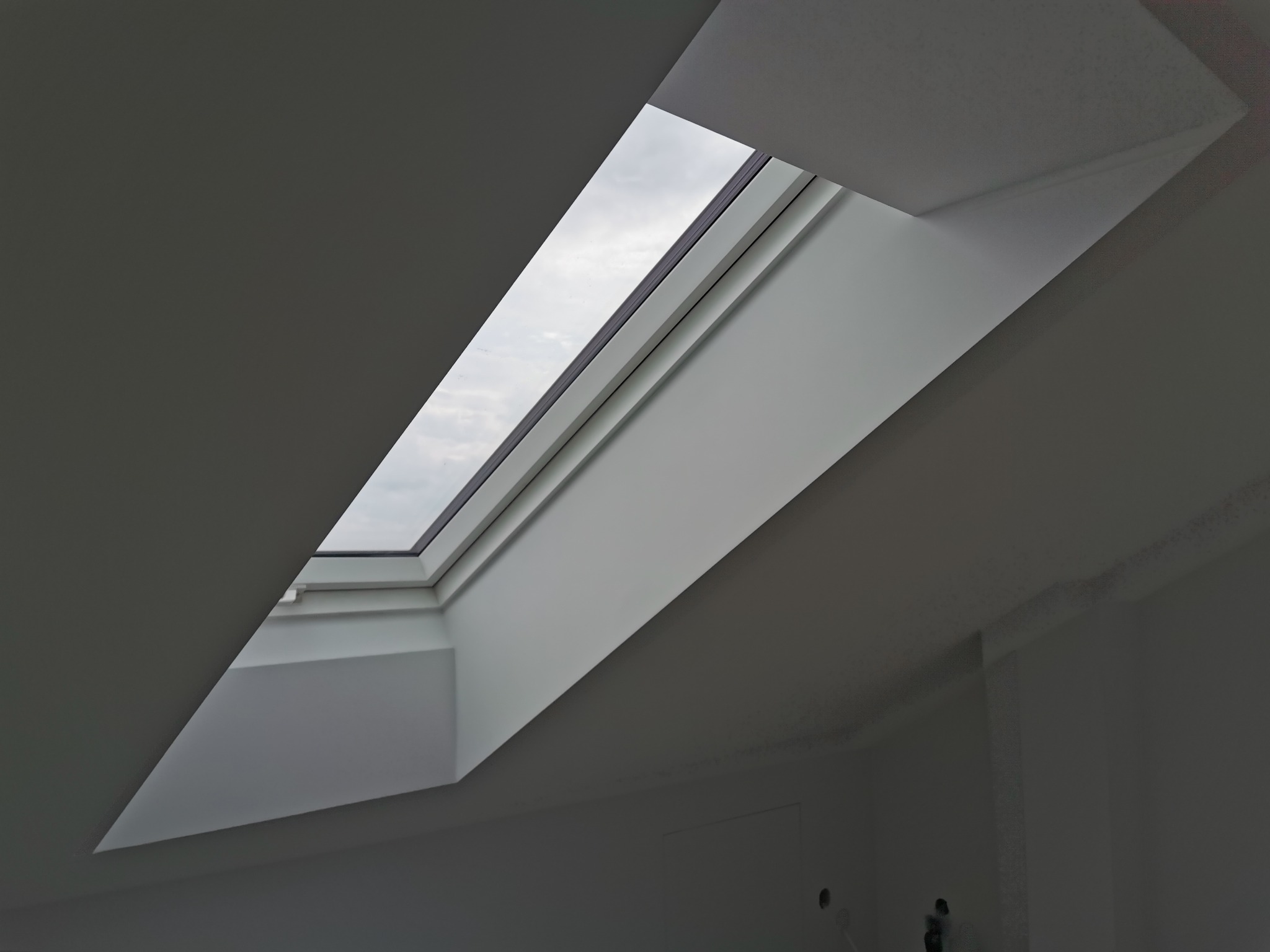 Wnętrze poddasza z oknem dachowym, świeżo pomalowane na biało, widoczne niedociągnięcia przy łączeniu ściany i dachu.