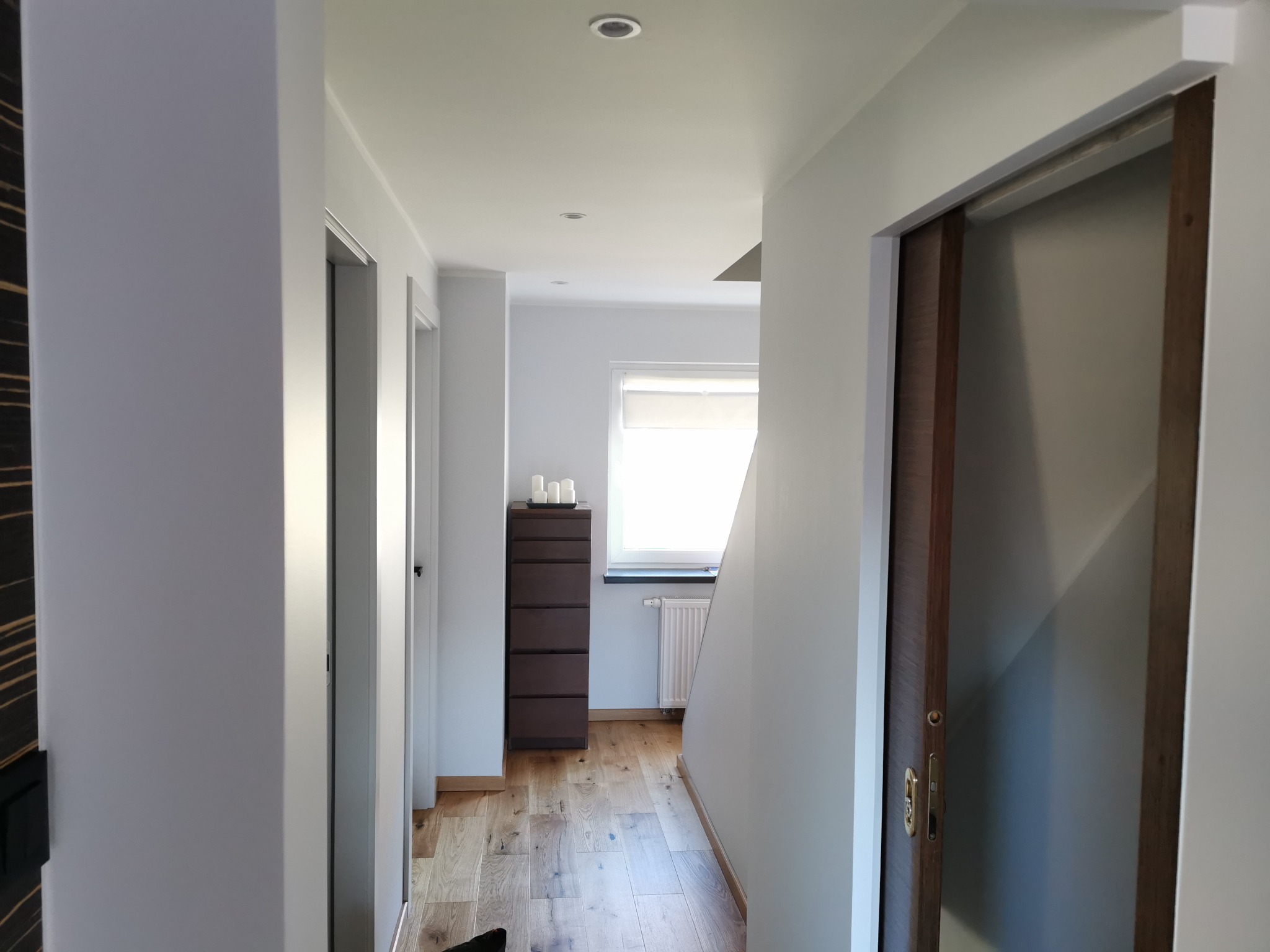 Korytarz w jasnych barwach z drewnianą podłogą, komodą i drzwiami przesuwnymi.