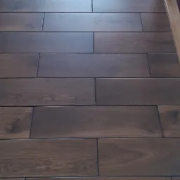 Ułożona podłoga z ciemnobrązowych płytek imitujących drewno, ułożonych w prostym wzorze, z widocznym odbiciem światła w górnej części kadru.