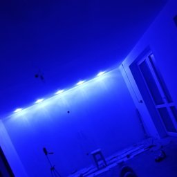 Remonty z klasą Grzegorz Dworecki - Niebieskie oświetlenie LED zamontowane pod sufitem w trakcie remontu, widoczny stołek, narzędzia i okno.