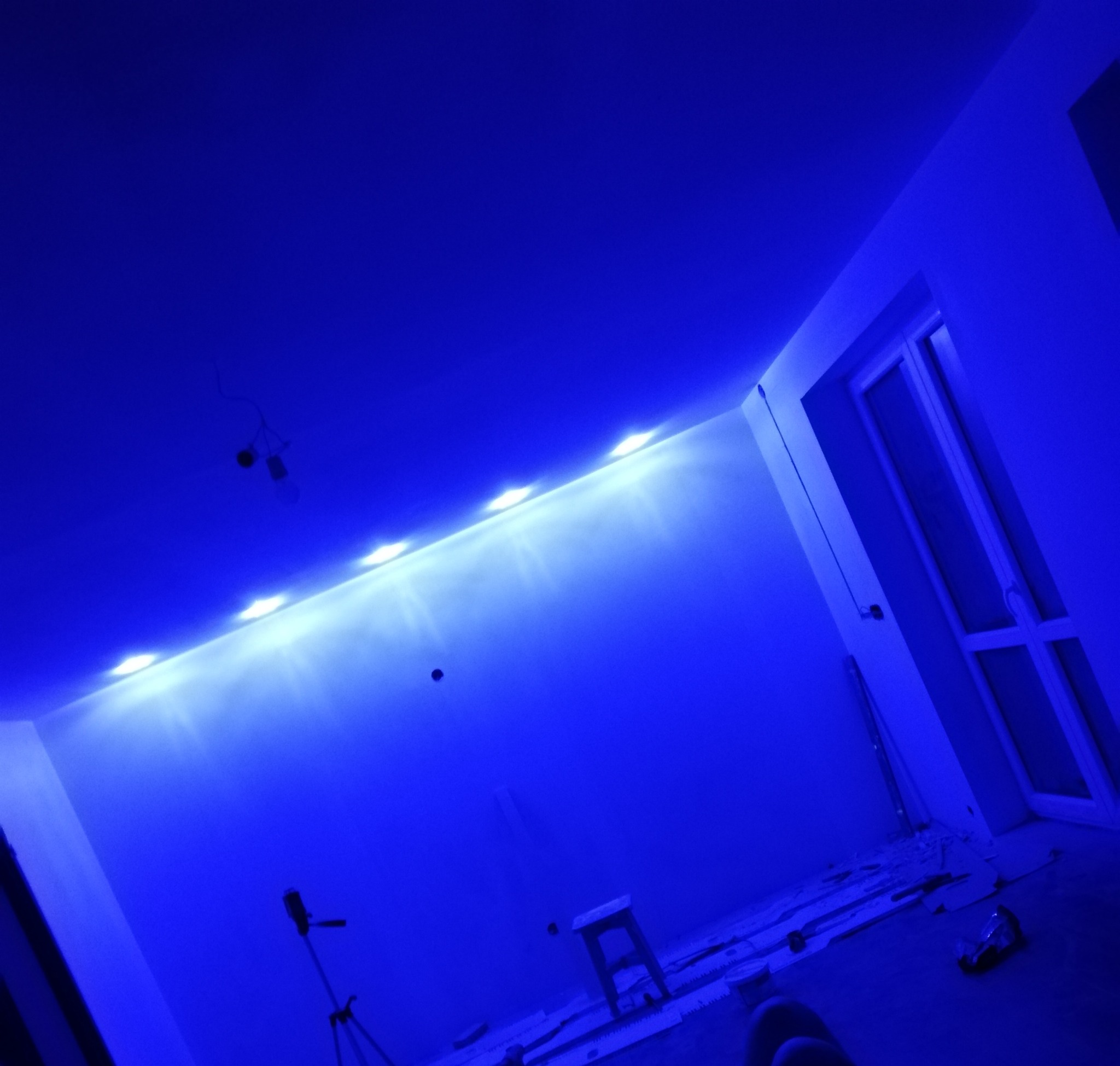 Niebieskie oświetlenie LED zamontowane pod sufitem w trakcie remontu, widoczny stołek, narzędzia i okno.