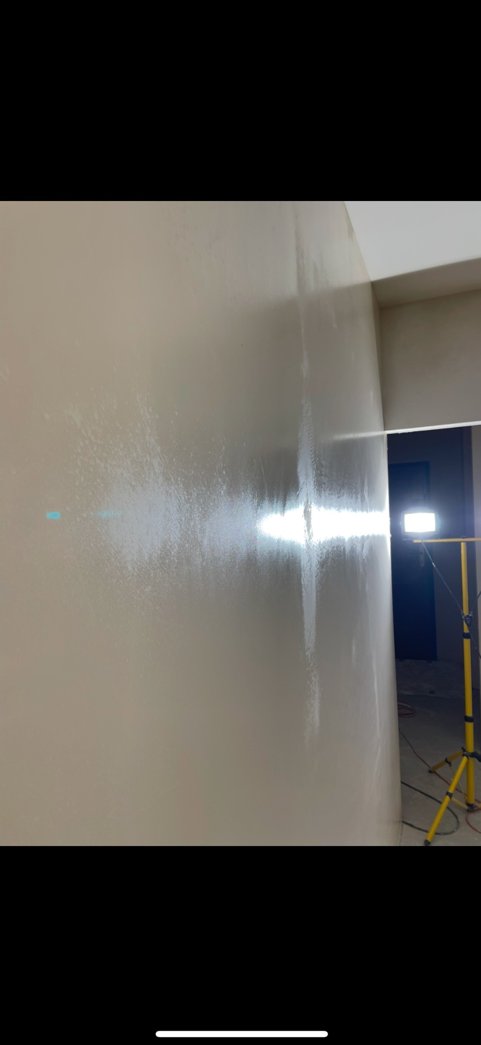 Ściana po malowaniu na jasny beż, widoczne smugi świeżej farby i lampa na statywie w rogu pomieszczenia. Świeżo pomalowane wnętrze.