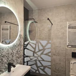 Wykończona łazienka z beżowymi płytkami, kabiną prysznicową z geometrycznym wzorem, okrągłym lustrem z podświetleniem LED, czarną armaturą i grzejnikiem drabinkowym.