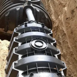 Czarny, modułowy tunel rozsączający Sicker-Tunnel 300, częściowo zakopany w wykopie z piasku, połączony z rurą kanalizacyjną, widok z góry.