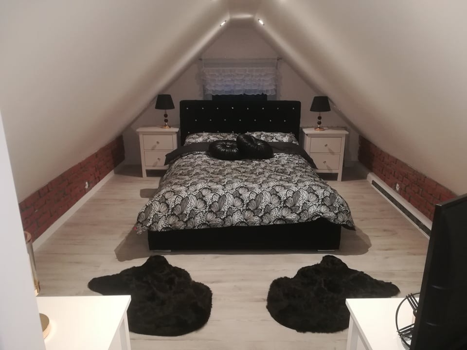 Pokój na poddaszu z łóżkiem, szafkami nocnymi i dekoracyjną ścianą z cegły, oświetlony lampkami nocnymi na złotych podstawach.