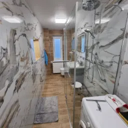 Wykończona łazienka w Wągrowcu z kabiną prysznicową typu walk-in, płytki imitujące marmur na ścianach, drewnopodobna podłoga oraz widoczne akcesoria łazienkowe.