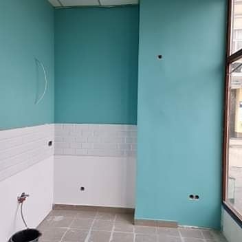 Świeżo pomalowane na turkusowo ściany pomieszczenia z częściowo ułożonymi białymi płytkami w stylu metro na dolnej części ściany. Widoczne przygotowania do montażu armatury i gniazdek elektrycznych.