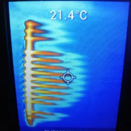 Termowizyjny obraz grzejnika żebrowego wskazujący temperaturę 21.4&deg;C, prezentowany na ekranie urządzenia pomiarowego.