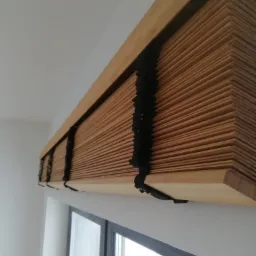 Zamontowane drewniane żaluzje poziome z czarnymi sznurkami w Olsztynie, widok z dołu, częściowo zasłonięte okno.