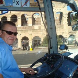 Barbara Ślesicka - Kierowca autobusu w okularach przeciwsłonecznych uśmiecha się, na tle Koloseum w Rzymie, widoczne przez szybę pojazdu.