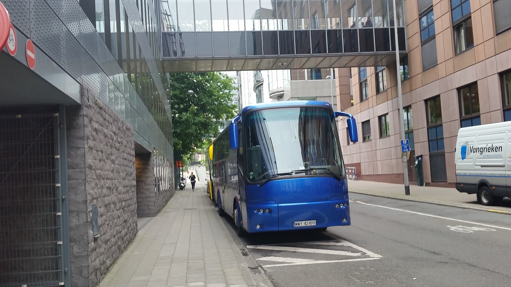 Niebieski autokar turystyczny zaparkowany przy chodniku w otoczeniu nowoczesnej architektury biurowej, z pieszą przechodzącą w oddali.