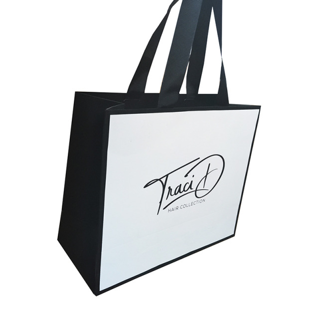 Elegancka, biało-czarna torba papierowa z logo 'Traci D HAIR COLLECTION' i czarnymi uchwytami, ustawiona pod kątem na białym tle.