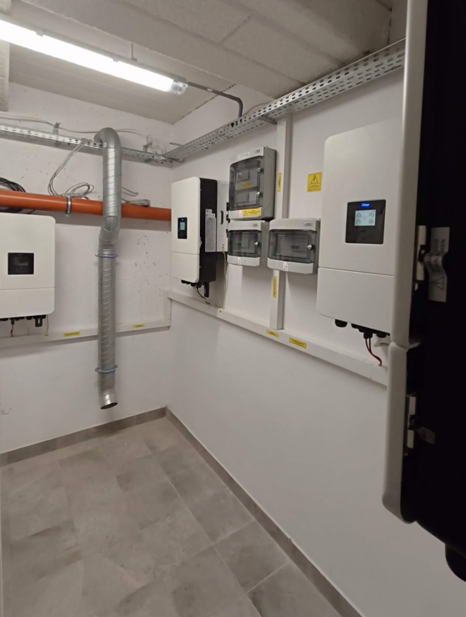 Wnętrze pomieszczenia technicznego z zamontowanymi urządzeniami: inwertery, rozdzielnice. Widoczne kable, rury wentylacyjne i elementy instalacji elektrycznej.