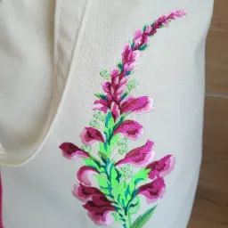 Ecru torba bawełniana z haftowanym motywem kwiatowym w odcieniach różu i zieleni, wykończona różową lamówką na górze.