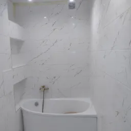 Biała wanna obudowana płytkami imitującymi marmur, z widoczną baterią i p&oacute;łkami w ścianie, w trakcie remontu łazienki, z niedokończonymi fugami i prowizorycznym oświetleniem.